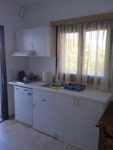 una cucina con armadi bianchi, lavandino e finestra di Iliachtida apartments a Philotium