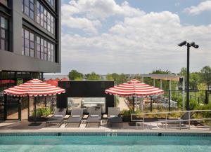 a swimming pool with chairs and umbrellas and a building at Roost Baltimore in Baltimore