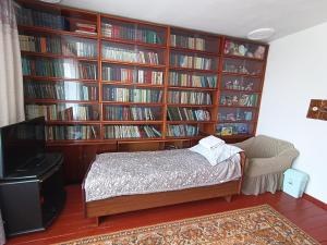 um quarto com uma parede de livros, uma cama e uma televisão. em Meerim Guest House em Bokonbayevo