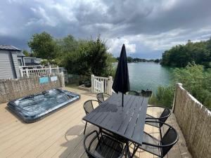 a wooden deck with a table and an umbrella at Lakeside Retreat 2 with hot tub, private fishing peg situated at Tattershall Lakes Country Park in Tattershall