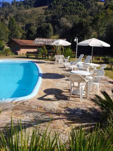a pool with white chairs and tables and umbrellas at Pousada Recanto da Vitória in Gonçalves