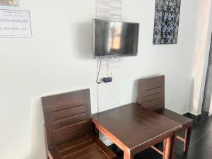 a wooden table and chair with a television on a wall at J2 INN in Uttaradit