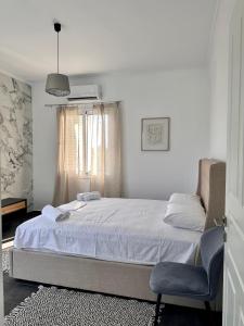 a white bedroom with a bed and a chair at Orange Grove Nafpaktos in Nafpaktos