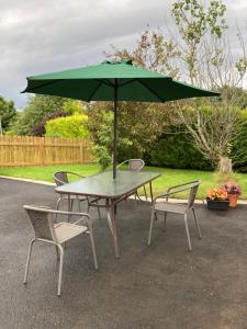 einen Tisch mit einem grünen Regenschirm und zwei Stühlen in der Unterkunft Willow Tree Cottage in Ballycastle