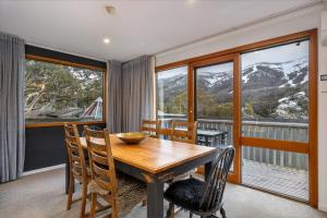 a dining room with a table and chairs and windows at Crackenback Castle free standing chalet with fire place in Thredbo