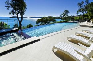 a swimming pool with lounge chairs and the water at Shorelines 27 Ocean View Buggy Transfers BBQ in Hamilton Island