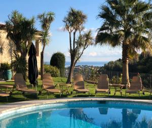 une piscine avec des chaises, des palmiers et une statue dans l'établissement Le Haut des Espinets, à Saint-Paul-de-Vence