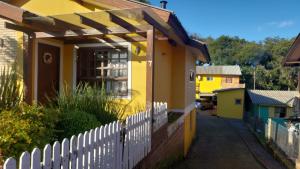 uma casa amarela com uma cerca branca à frente. em Jardim Temporadas em Canela