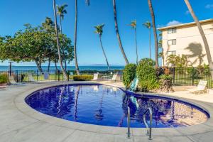 a swimming pool with palm trees and the ocean in the background at Kanai A Nalu 214 in Wailuku