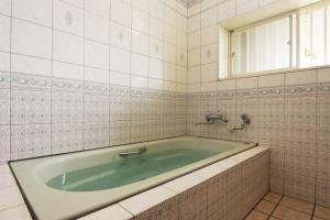 a bath tub in a white tiled bathroom at 民宿やまそ in Takashima