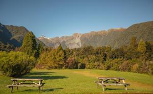 two picnic tables in a field with mountains in the background at Rainforest Motel in Fox Glacier