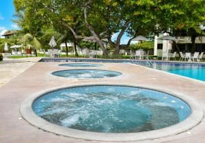 a pool with three jacuzzi pools with tables and chairs at Carneiros Beach Resort - Flats Cond à Beira Mar in Praia dos Carneiros