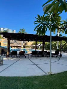 a group of chairs and tables under a pavilion with a palm tree at Departamento de lujo. Seguridad 24. Playa a pasos. in Acapulco
