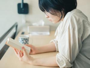 een vrouw aan een tafel die een boek leest bij Kagan Hotel & Hostel in Kyoto