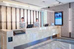 two men standing behind a reception desk in a lobby at Atour X Hotel Shenyang Beiling Park in Shenyang