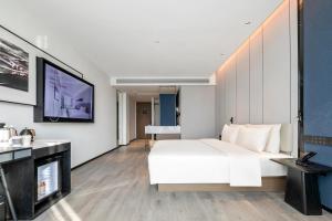 1 dormitorio con cama blanca y TV en la pared en Atour Hotel Huaihua High-Speed South Railway Station en Huaihua