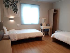 1 dormitorio con 2 camas, ventana y escritorio en Uniqstay, en Busan
