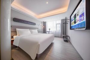 Cette chambre comprend un lit blanc et une télévision à écran plat. dans l'établissement Atour Light Hotel Huizhou Jinshanhu Ganghui, à Huizhou
