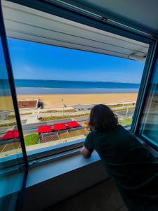 uma pessoa olhando para fora de uma janela na praia em La Maison Régent & spa face à la mer em Pornichet