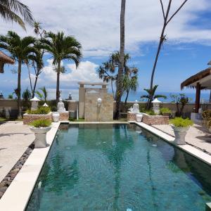 a swimming pool with palm trees and the ocean in the background at Puri Mas Boutique Resort & Spa in Senggigi