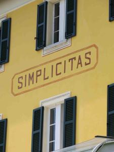 a sign on the side of a yellow building with windows at Hotel Villa Simplicitas in San Fedele Intelvi