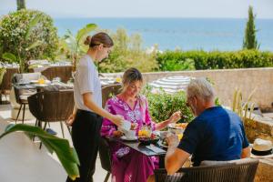 a woman talking to two people sitting at a table at Royal Apollonia by Louis Hotels in Limassol