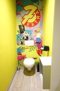 La salle de bains est pourvue de toilettes et d'un mur jaune. dans l'établissement Capsule 90's - Jacuzzi - Sauna - Flipper - Billard - Netflix - Nintendo Switch & Jeux -, à Mons
