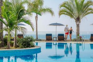Ein Mann und eine Frau stehen neben einem Pool mit Palmen. in der Unterkunft Royal Apollonia by Louis Hotels in Limassol