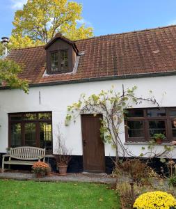 une maison blanche avec une porte en bois et un banc dans l'établissement Perlefien, à Zottegem