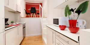 Precioso apartamento en Calle Iriarte في مدريد: مطبخ مع خزائن بيضاء و مزهريات حمراء