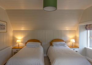 twee bedden in een kleine kamer met twee lampen bij Duart Cottage in Glencoe