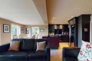 a living room with a black couch and a kitchen at Pen Y Bryn in Llanrwst
