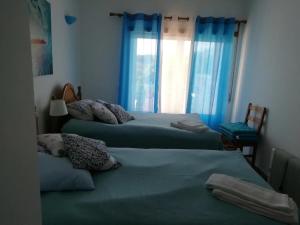 1 dormitorio con 2 camas y una ventana con cortinas azules en Brisamar, en Aljezur