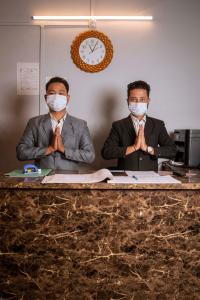 Dois homens com máscaras faciais sentados numa secretária. em Shree Krishna GH em Guwahati