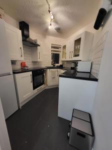 Lovely 2-Bed Apartment in Grays في South Ockendon: مطبخ بدولاب بيضاء وأرضية سوداء