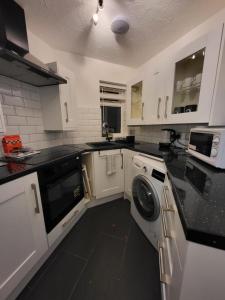 Lovely 2-Bed Apartment in Grays في South Ockendon: مطبخ مع دواليب بيضاء وغسالة ونشافة