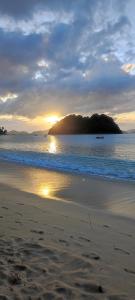 a sunset on a beach with a island in the water at ALFA Garden Lodge in El Nido