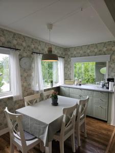 eine Küche mit einem weißen Tisch, Stühlen und Fenstern in der Unterkunft Mysig stuga i naturskönt område. in Vetlanda