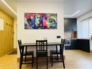 a dining room table with chairs and a painting on the wall at Alto Turtas Apartamentai in Šiauliai