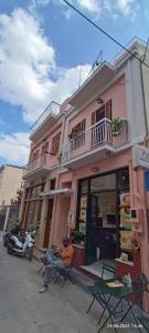 a man sitting in a chair in front of a pink building at Lefterakis place in Egina