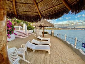una playa con sillas blancas, sombrilla de paja y agua en Departamento junto a las hadas manzanillo en Manzanillo