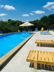 a swimming pool with benches and an umbrella at Vita Gardenia Hotel Tskaltubo in Tsqaltubo