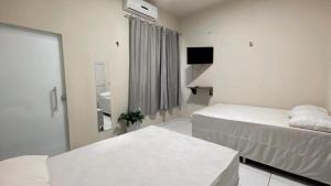 a white room with two beds and a television at Pousada Villa Rica in Carolina