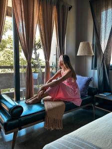 een jong meisje op een bed dat uit het raam kijkt bij Kaia Gallery Hotel Hoi An in Hội An