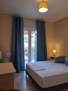1 dormitorio con 1 cama con cortinas azules y ventana en Margaret's House, en Cefalonia