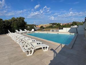 a row of white lounge chairs next to a swimming pool at Apartman SeaSide 8 in Banjole