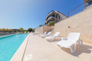 a pool with white lounge chairs next to a brick wall at Apartman Seaside 5 in Banjole