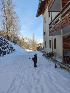 un niño pequeño parado en la nieve fuera de una casa en 2 pièces Valloire pied des pistes en Valloire