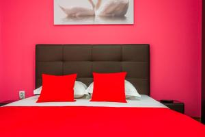a bed with two red pillows and a pink wall at Pensiunea Aura in Murighiol