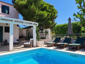 a pool with chairs and an umbrella next to a house at Holiday home Voga in Maslinica